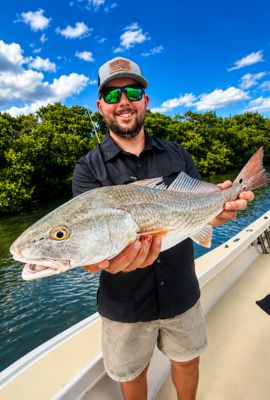 Man holding a redfish on a Florida fishing charter boat with mangroves and blue water in the background
